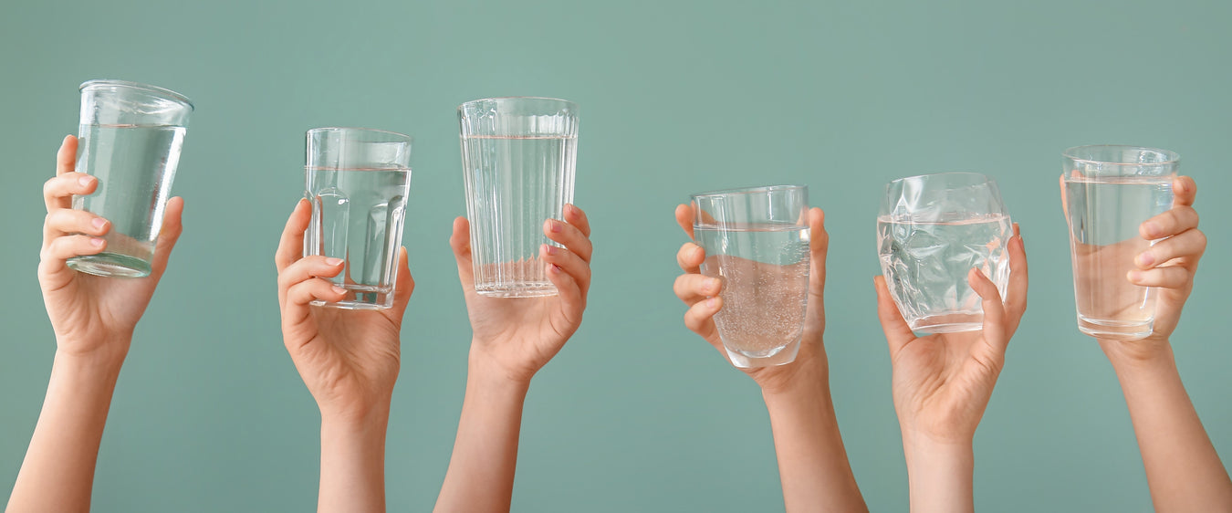 Vannrensing - hender som holder glass med rent vann