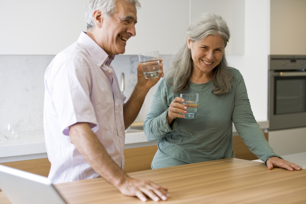 Eldre par drikker vann på kjøkkenet